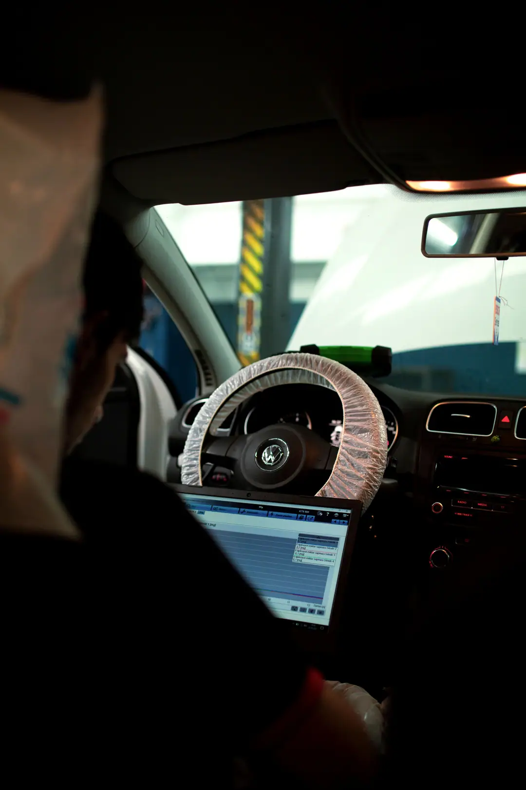 Technicien de dos assis au volant, ordinateur portable relié au véhicule affichant des courbes de diagnostic électronique