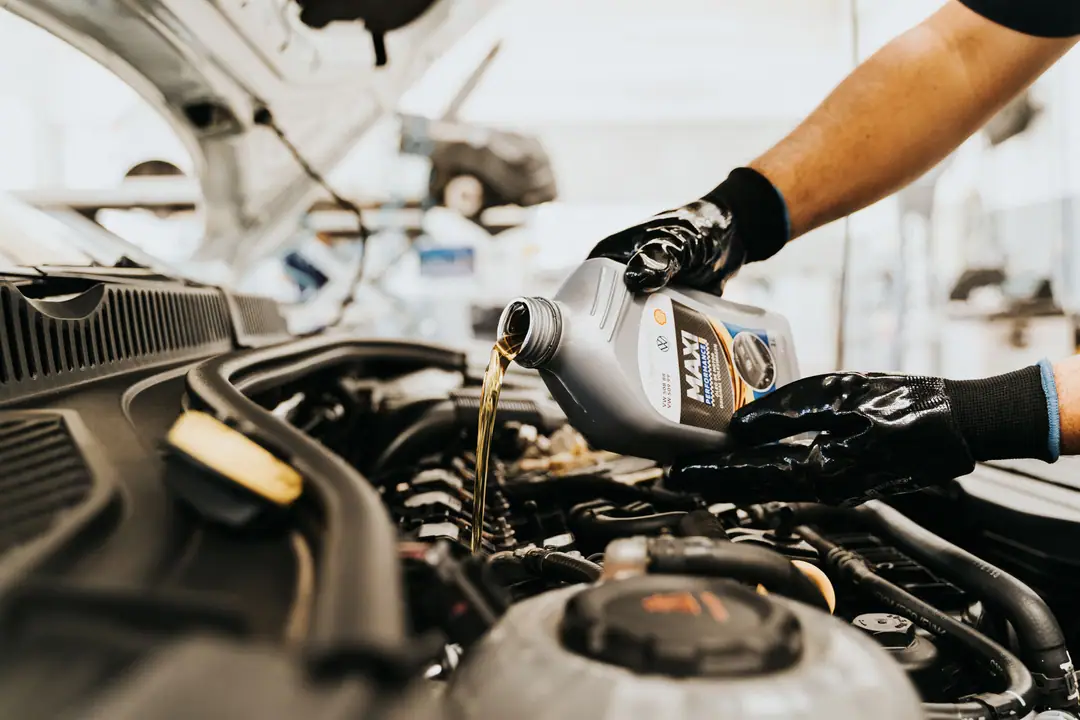 Mains gantées versant de l'huile moteur neuve dans l'orifice de remplissage d'un moteur, pendant une vidange en atelier