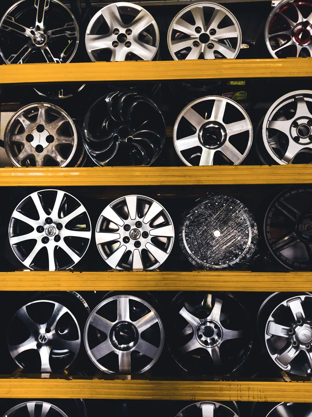 Jantes en alliage de différents modèles alignées sur des rayonnages noirs et jaunes, dans un magasin de pièces automobiles
