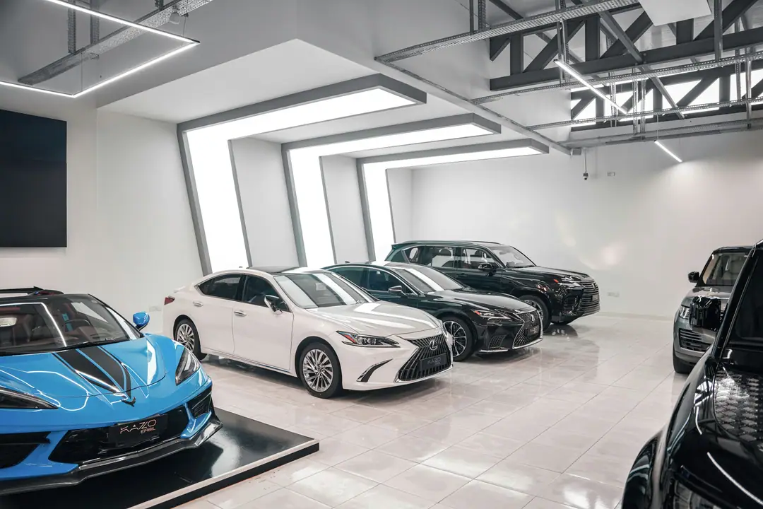 Showroom blanc et lumineux où sont alignées des voitures haut de gamme, dont un coupé sportif bleu et plusieurs berlines